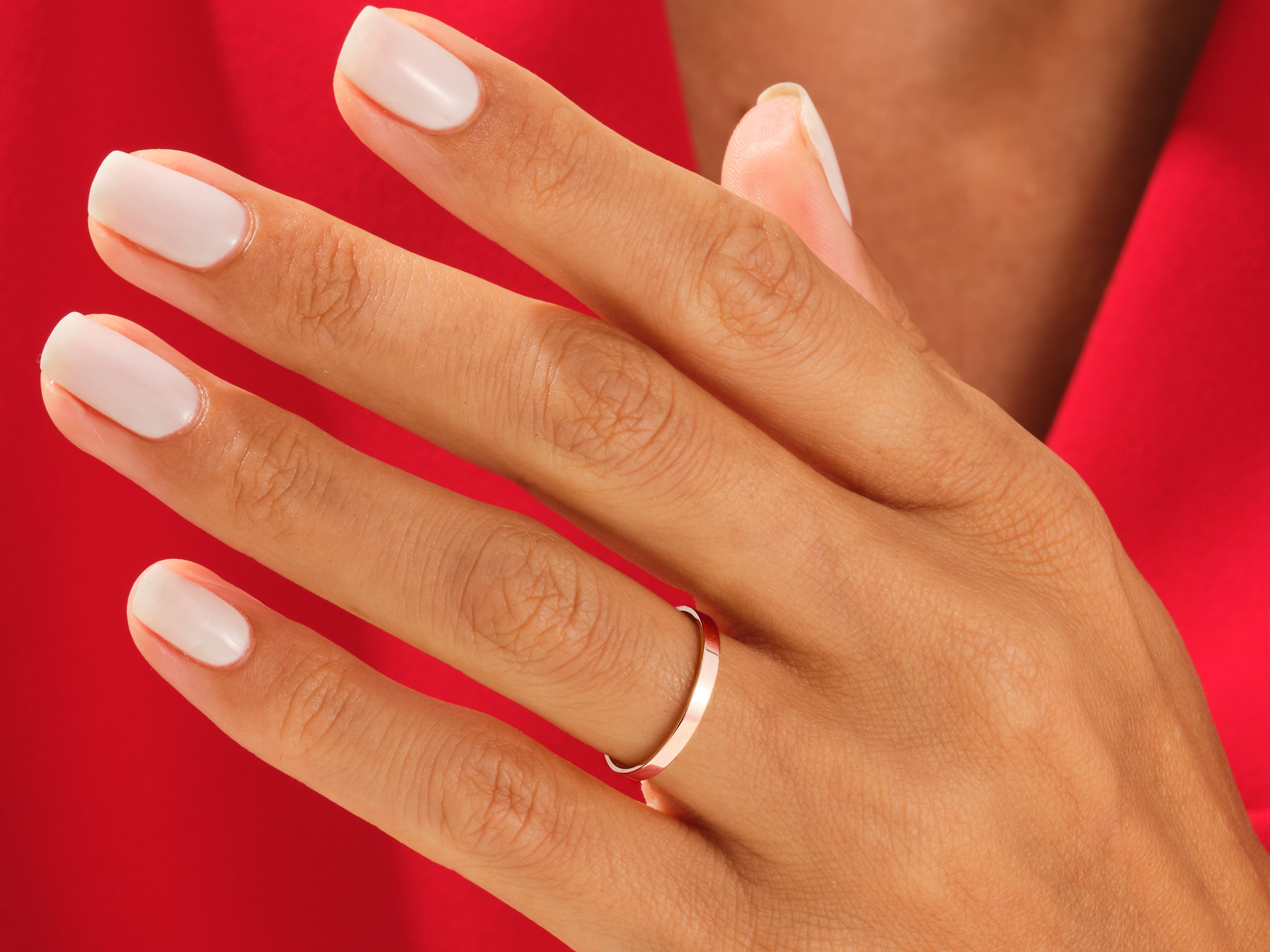 Rose gold band ring on a hand with white nails