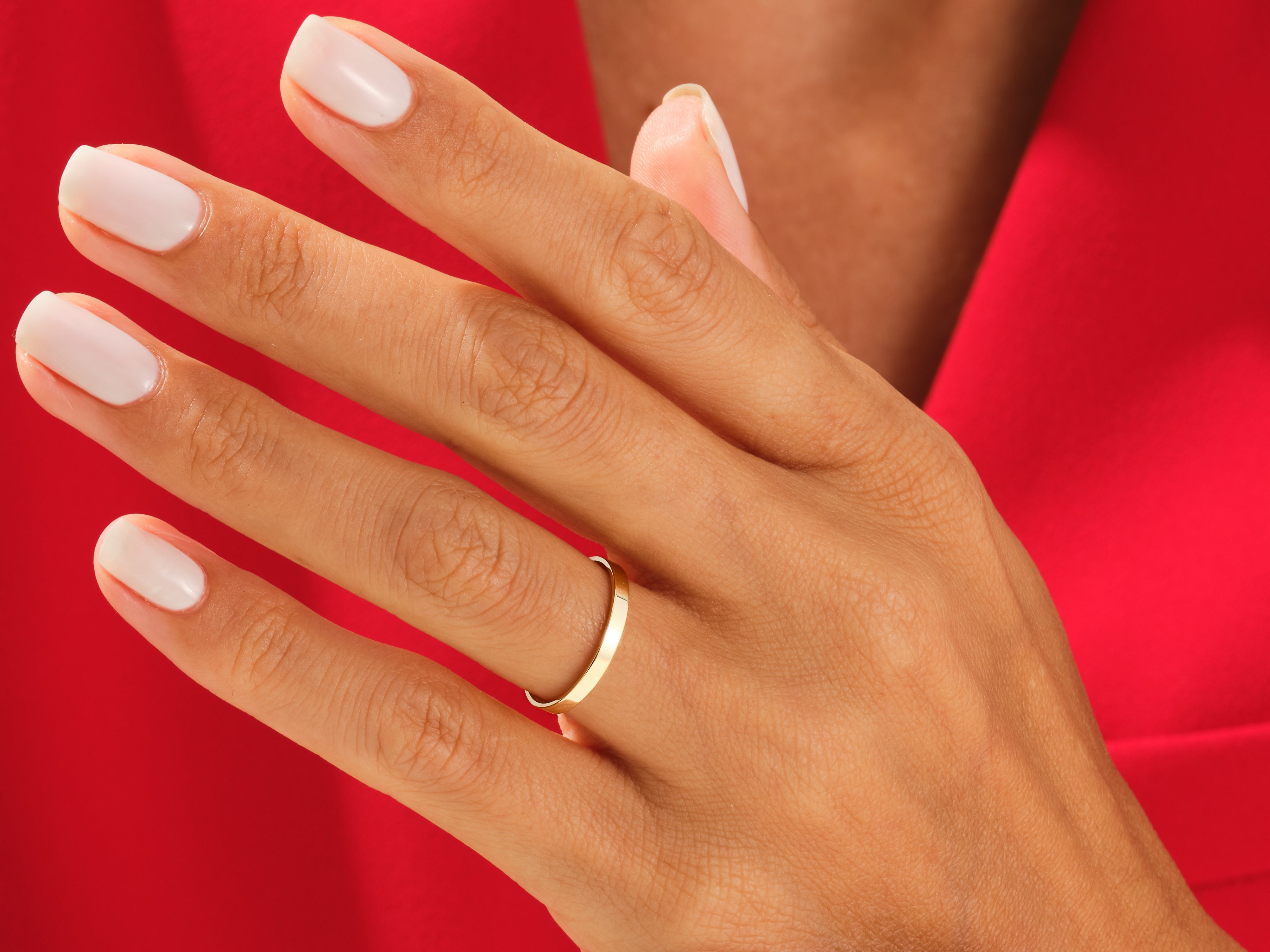 Gold wedding band on hand with white nails, jewelry product