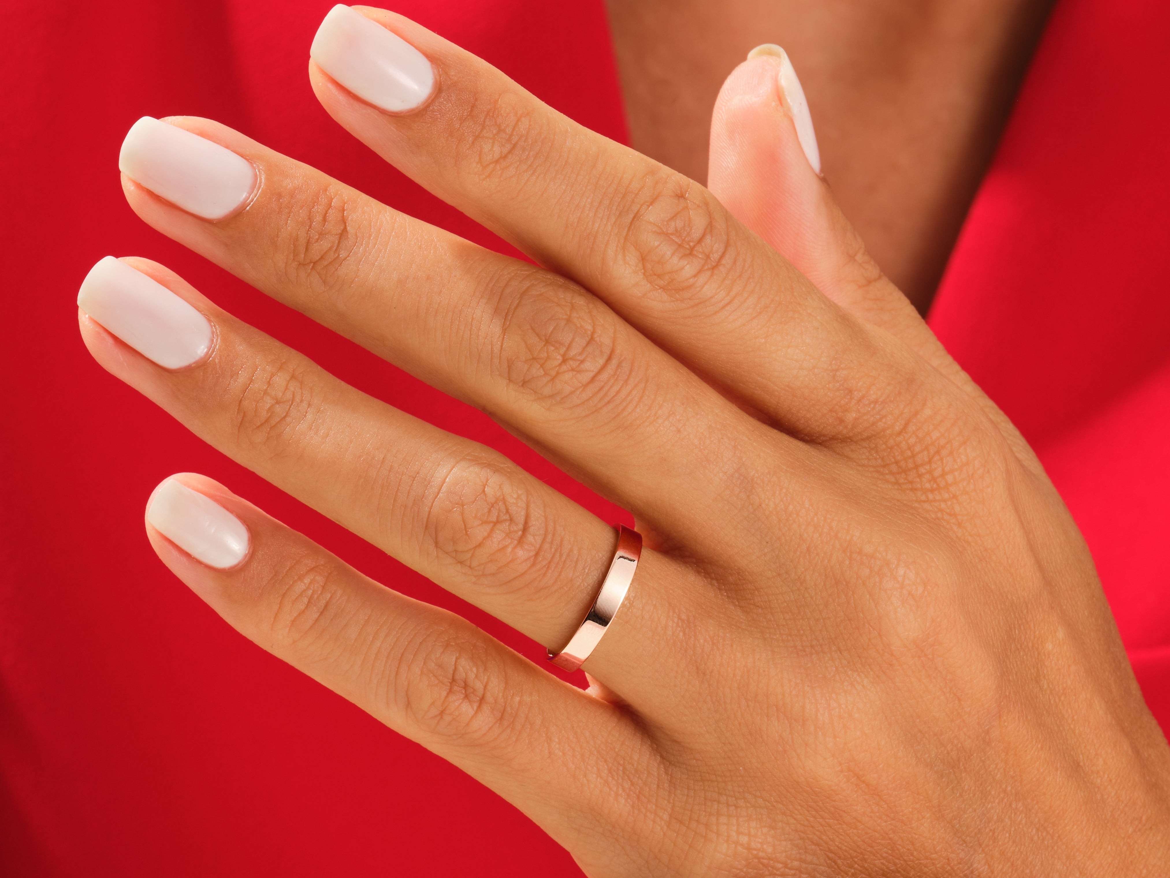 Rose gold wedding band on a hand with white nails