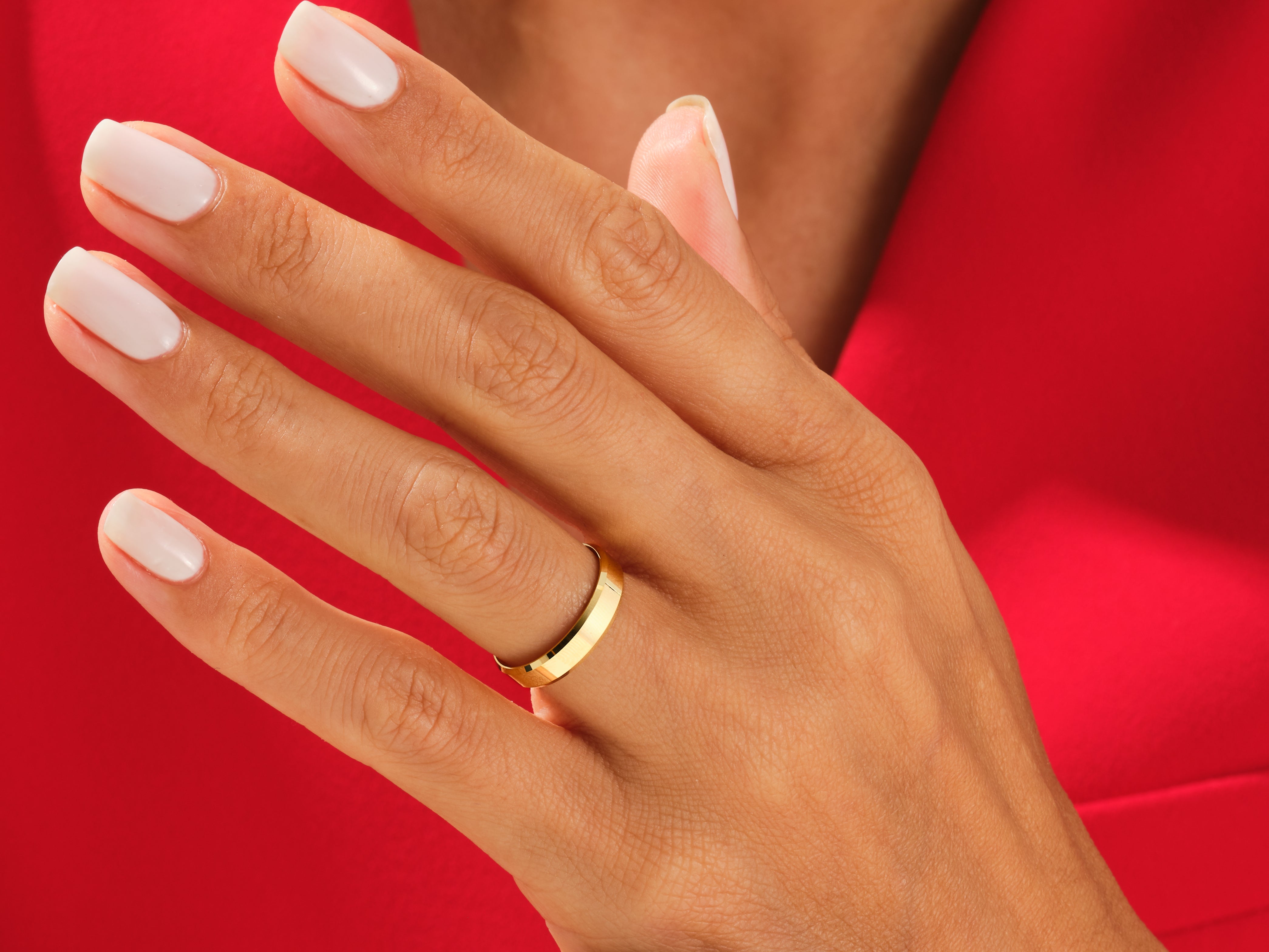 Gold wedding band on a hand with white nails, jewelry