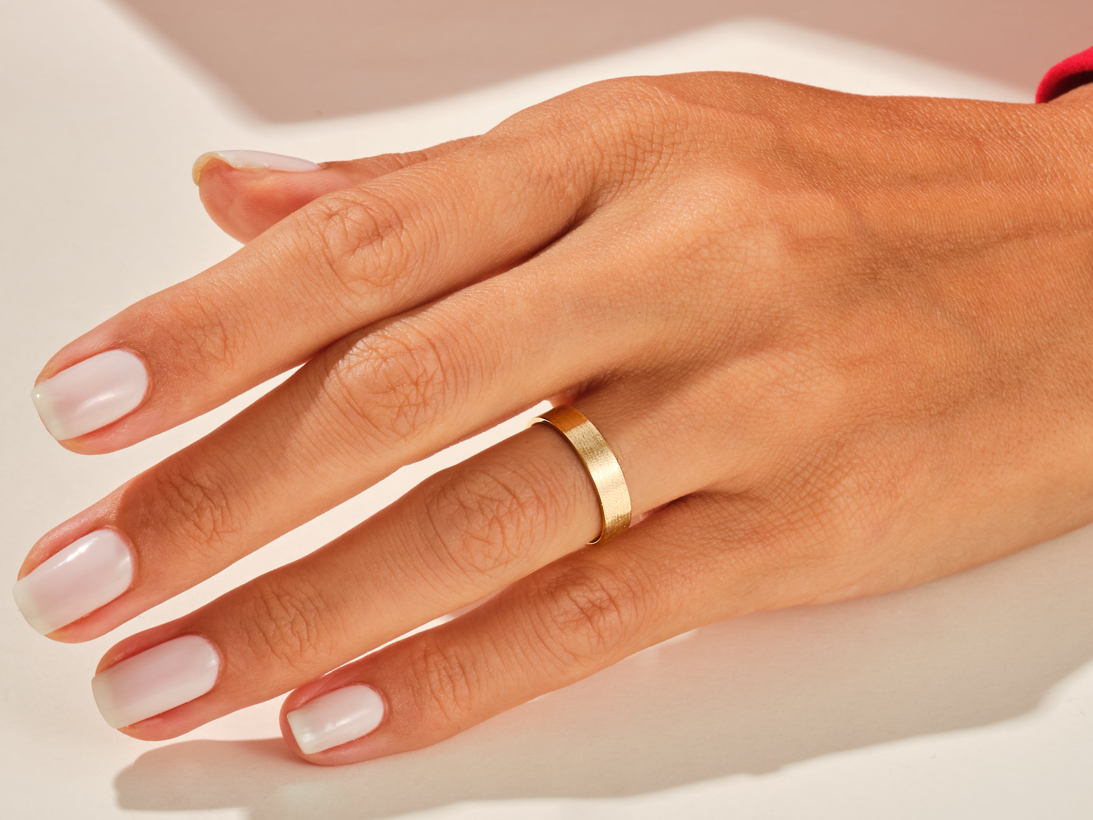 Gold band ring on a hand with manicured nails