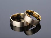 Two brushed gold wedding rings on a reflective surface