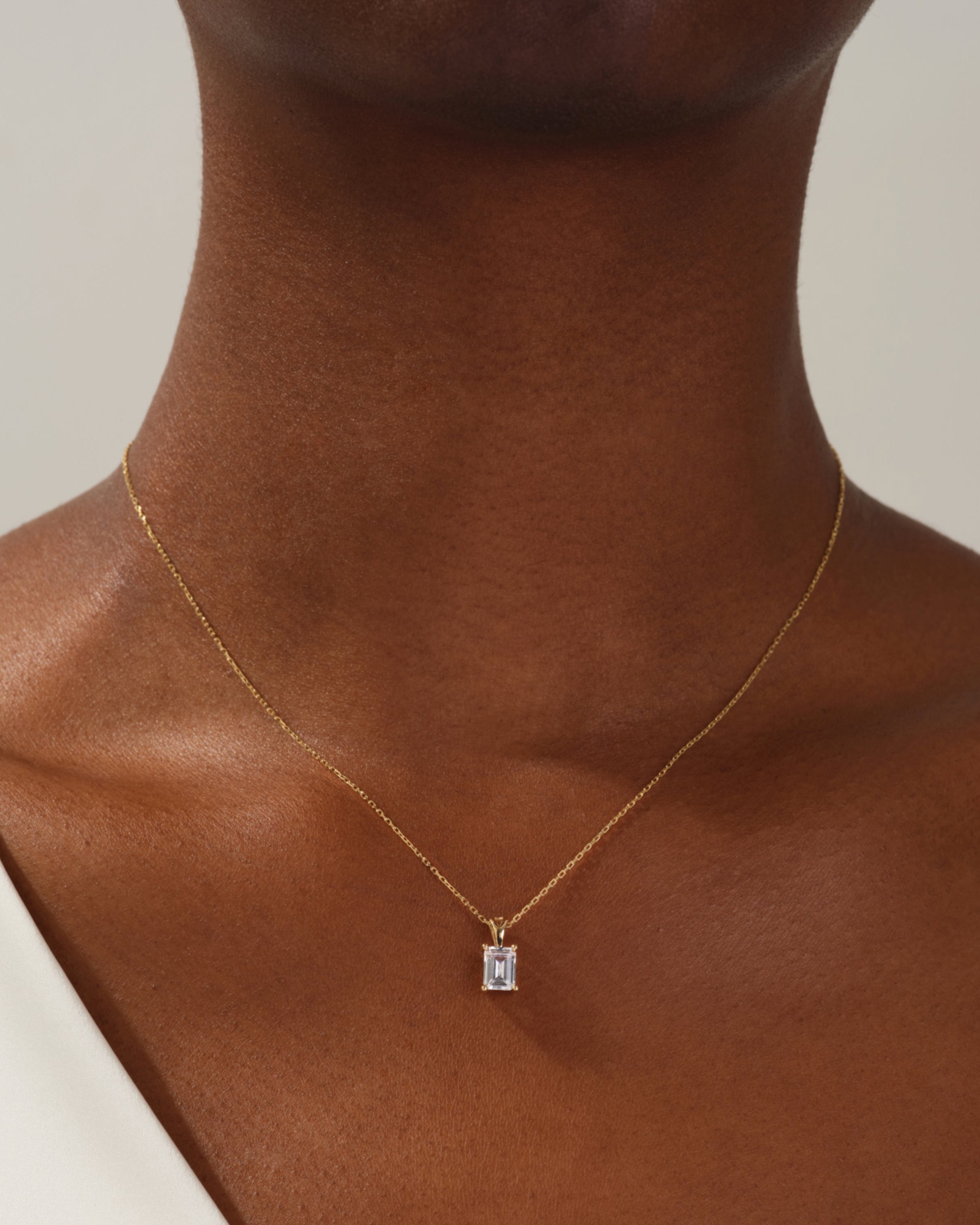 Gold necklace with emerald-cut diamond pendant on a woman's neck