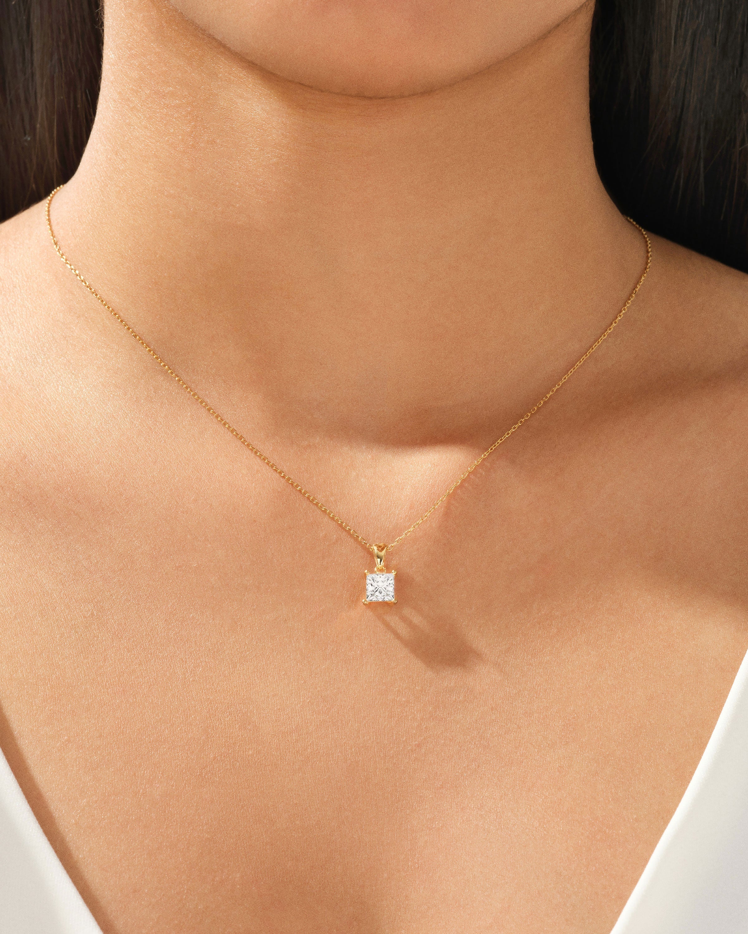 Gold necklace with princess cut diamond pendant on a woman's neck