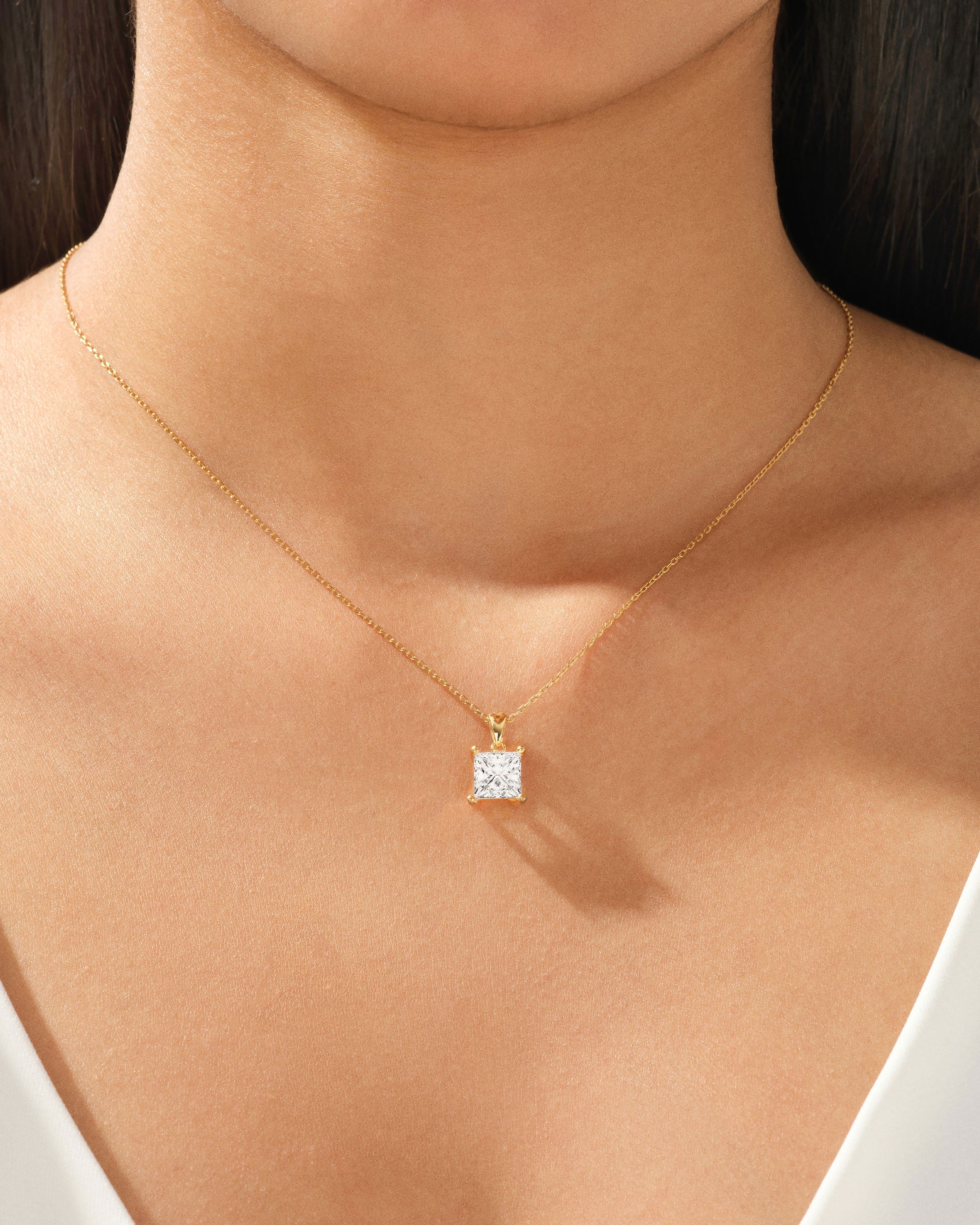 Gold necklace with princess cut diamond pendant on a woman's neck