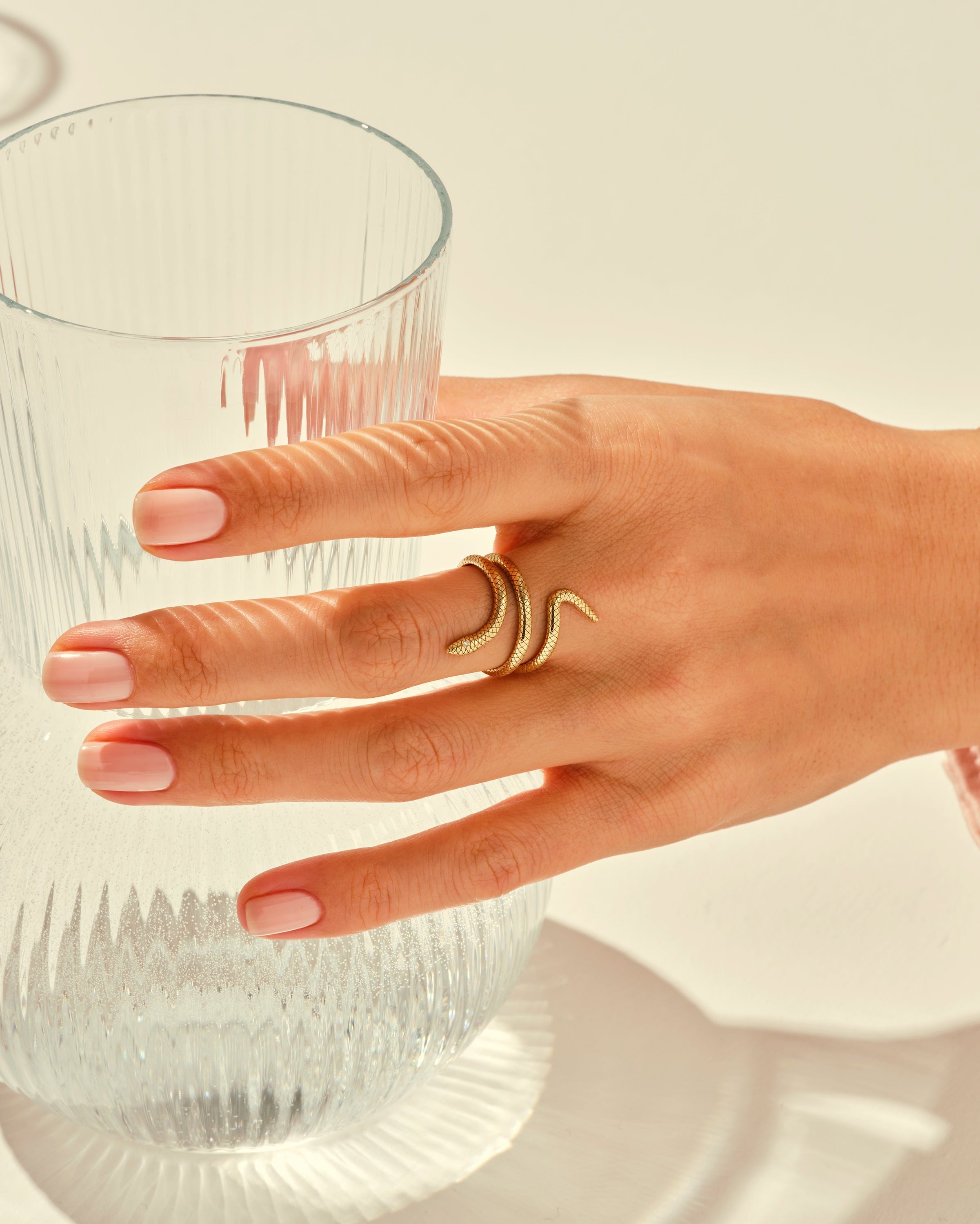 Gold snake ring on hand near elegant glassware