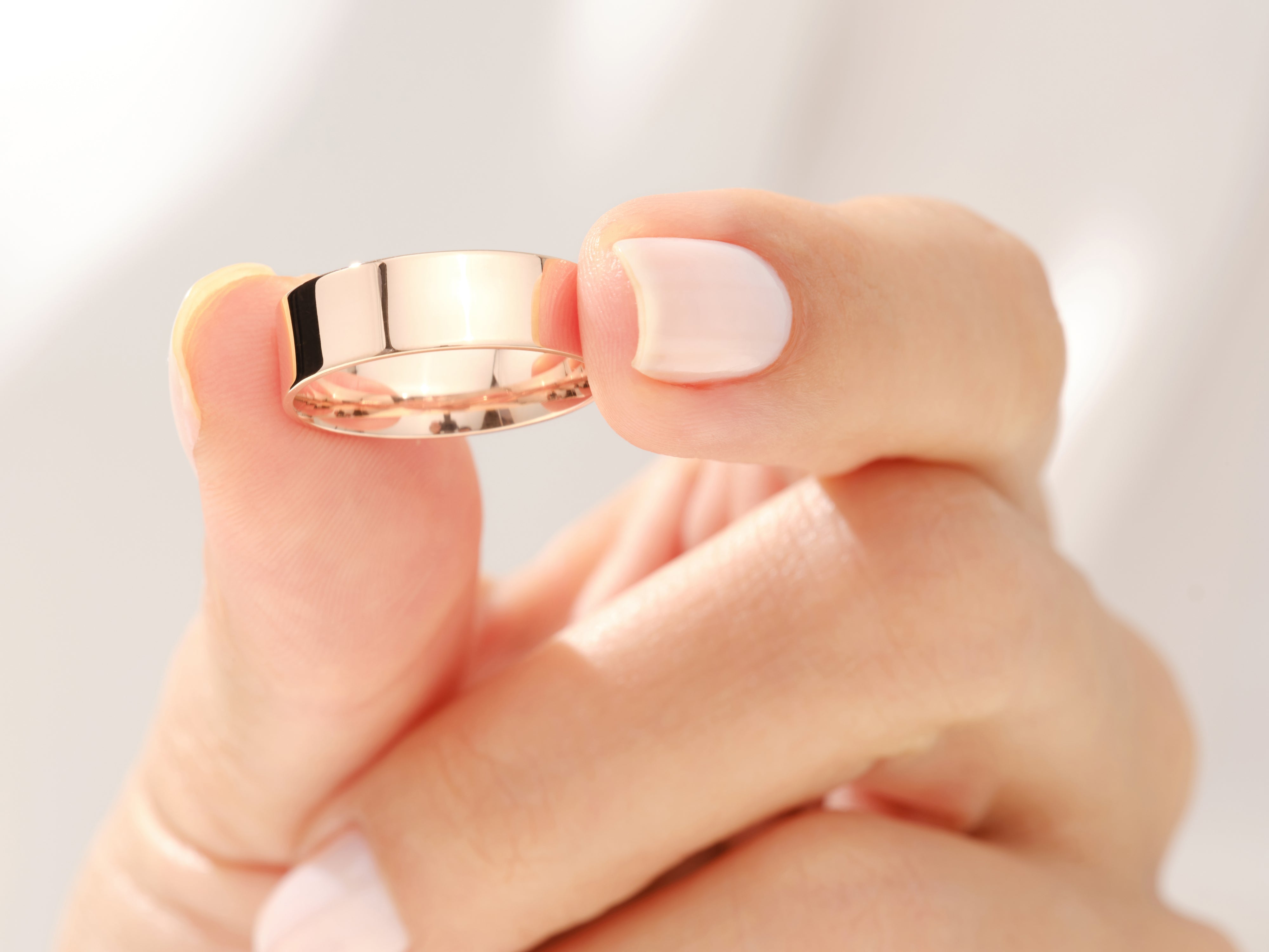 Rose gold wedding band held by manicured fingers, jewelry photography
