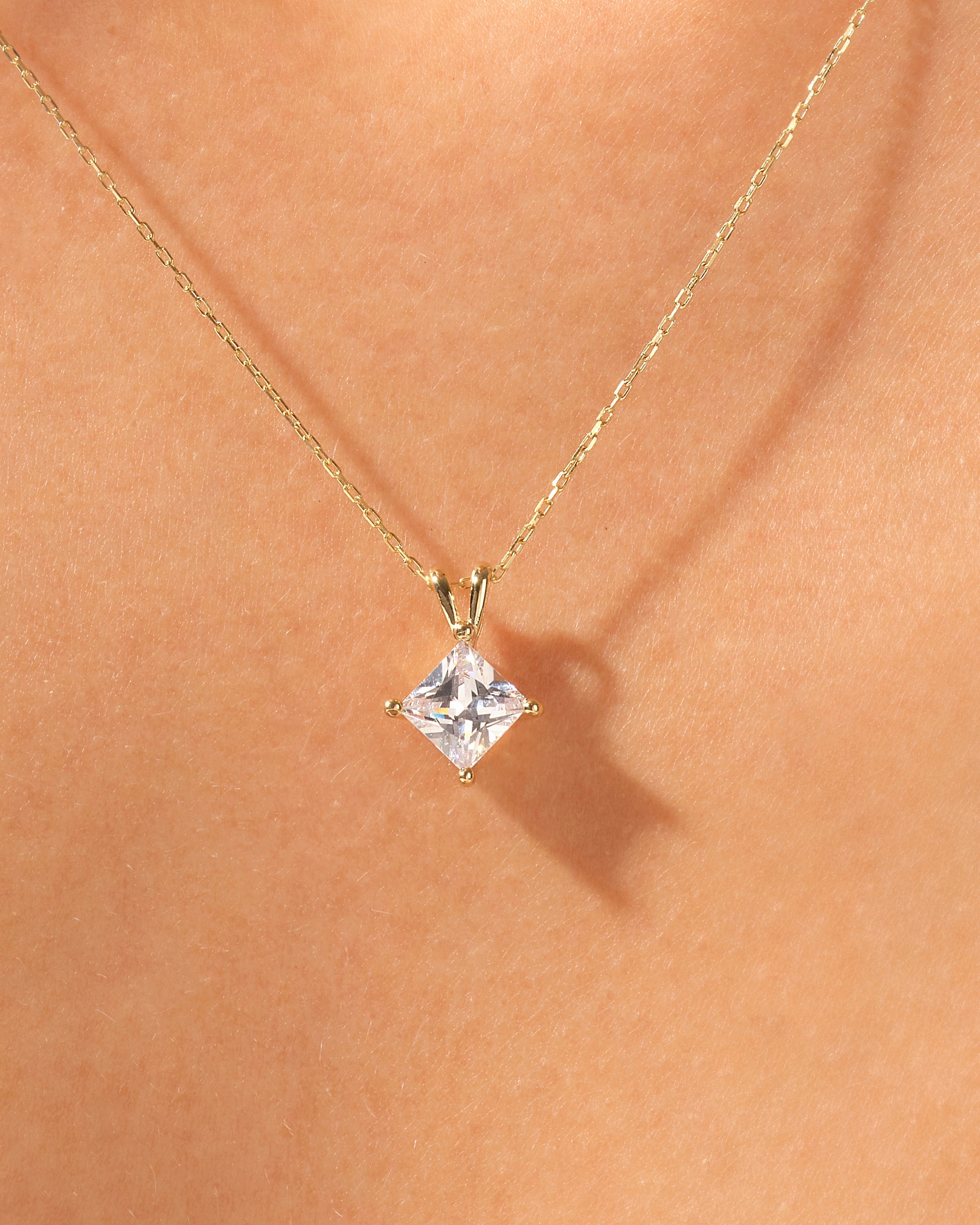 Gold necklace with princess cut diamond pendant on skin